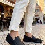 Men's black slip-on loafers with side stitching, worn with light pants
