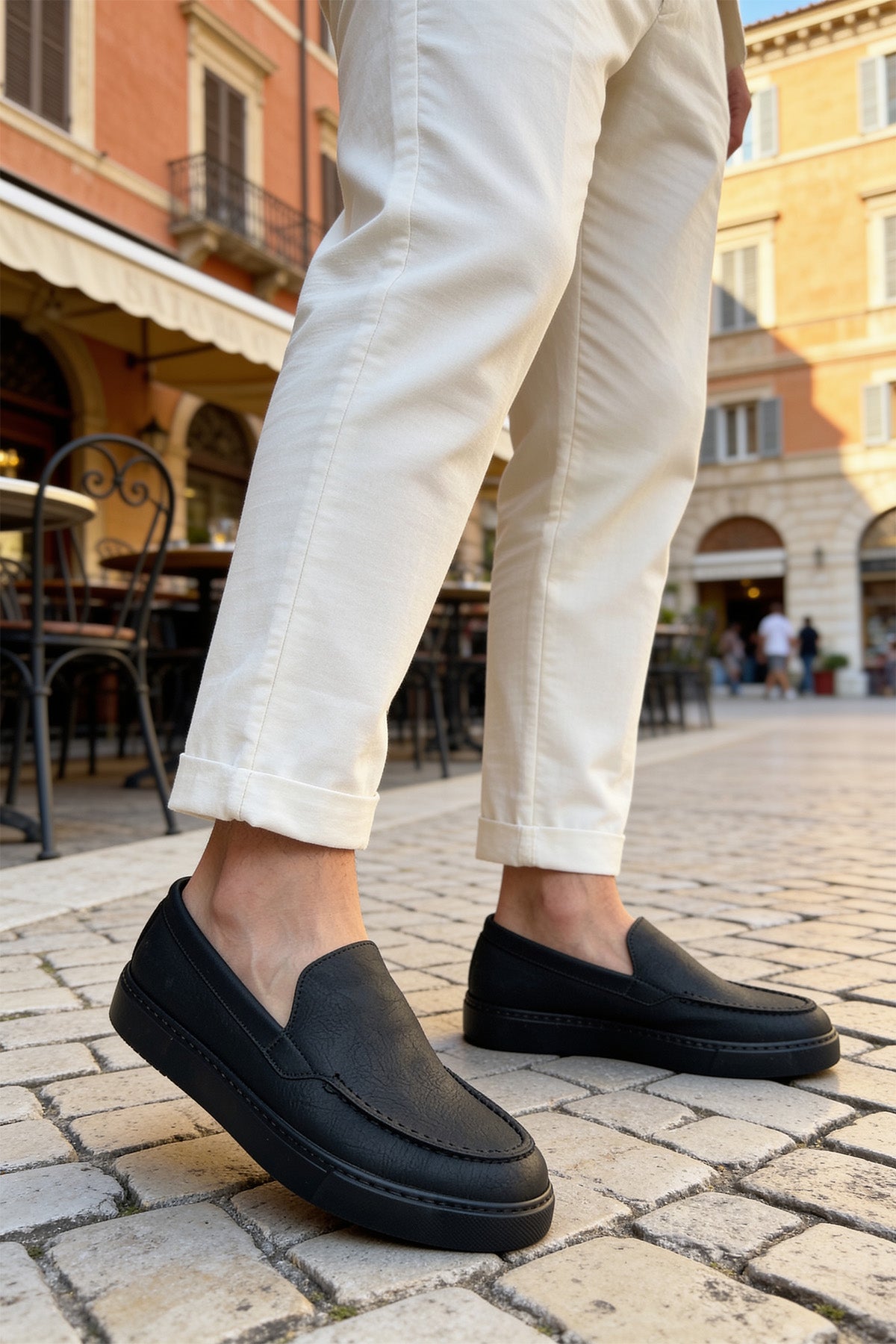 Men's black slip-on loafers with side stitching, worn with light pants