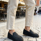Pair of men's black loafers with moc-style stitching, worn with light trousers