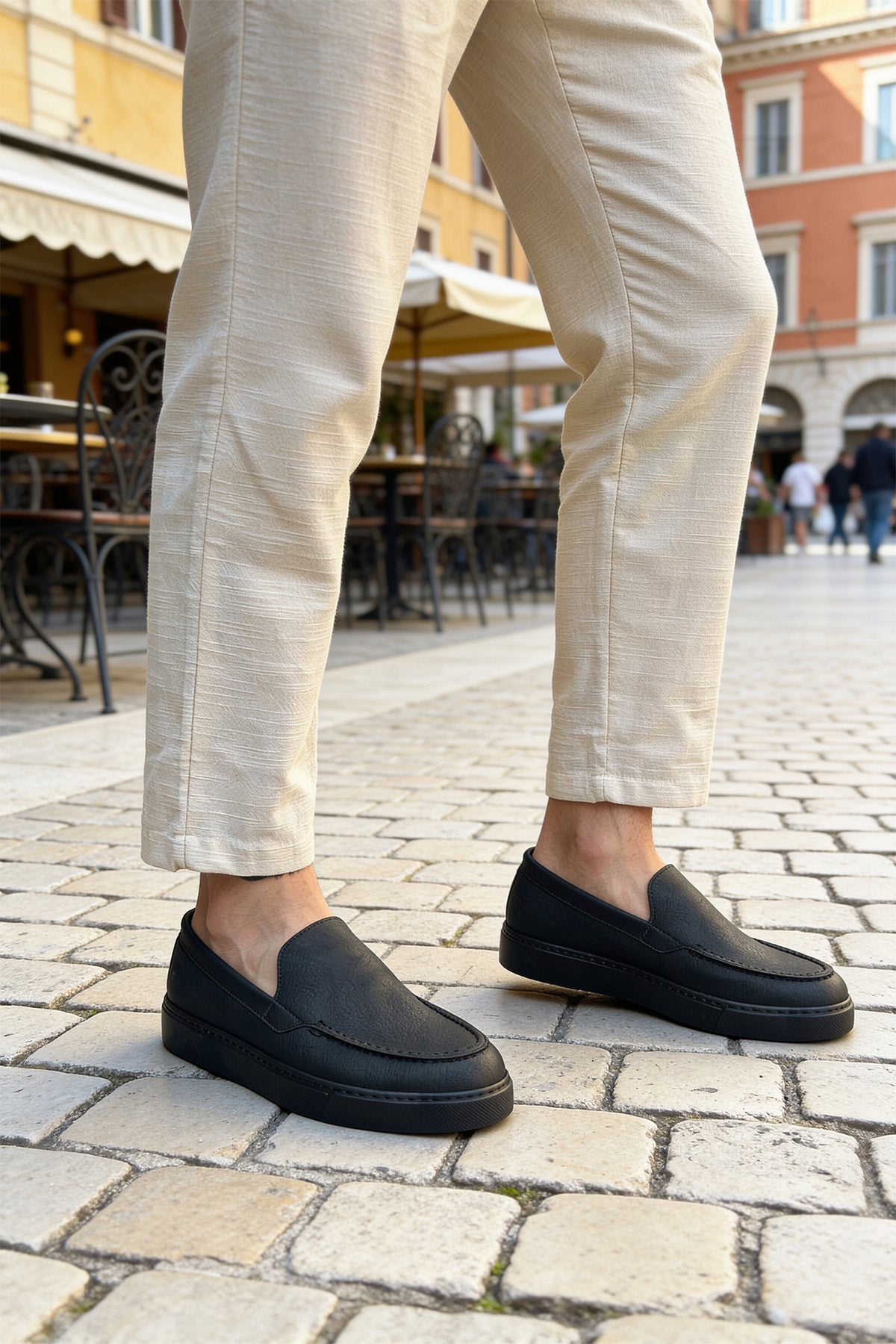 Pair of men's black loafers with moc-style stitching, worn with light trousers