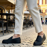 Men's black loafers on cobblestone, front view with light pants
