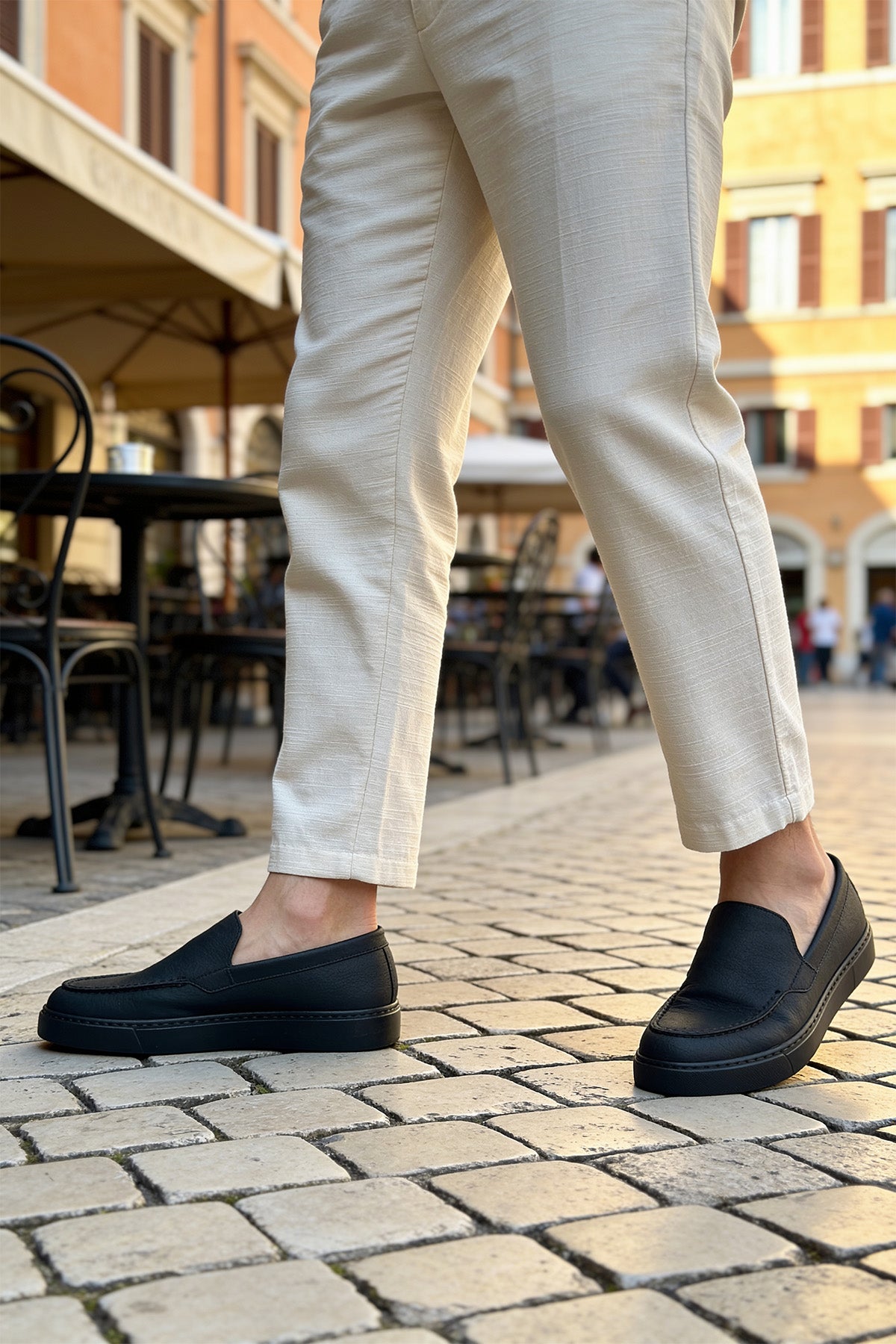 Men's black loafers on cobblestone, front view with light pants