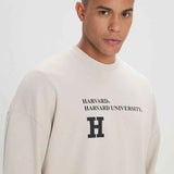 Beige oversized sweatshirt with Harvard chest logo, close-up