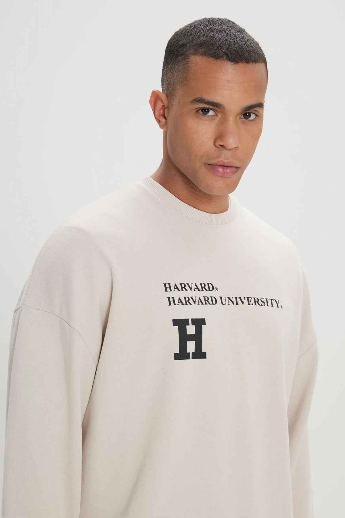 Beige oversized sweatshirt with Harvard chest logo, close-up