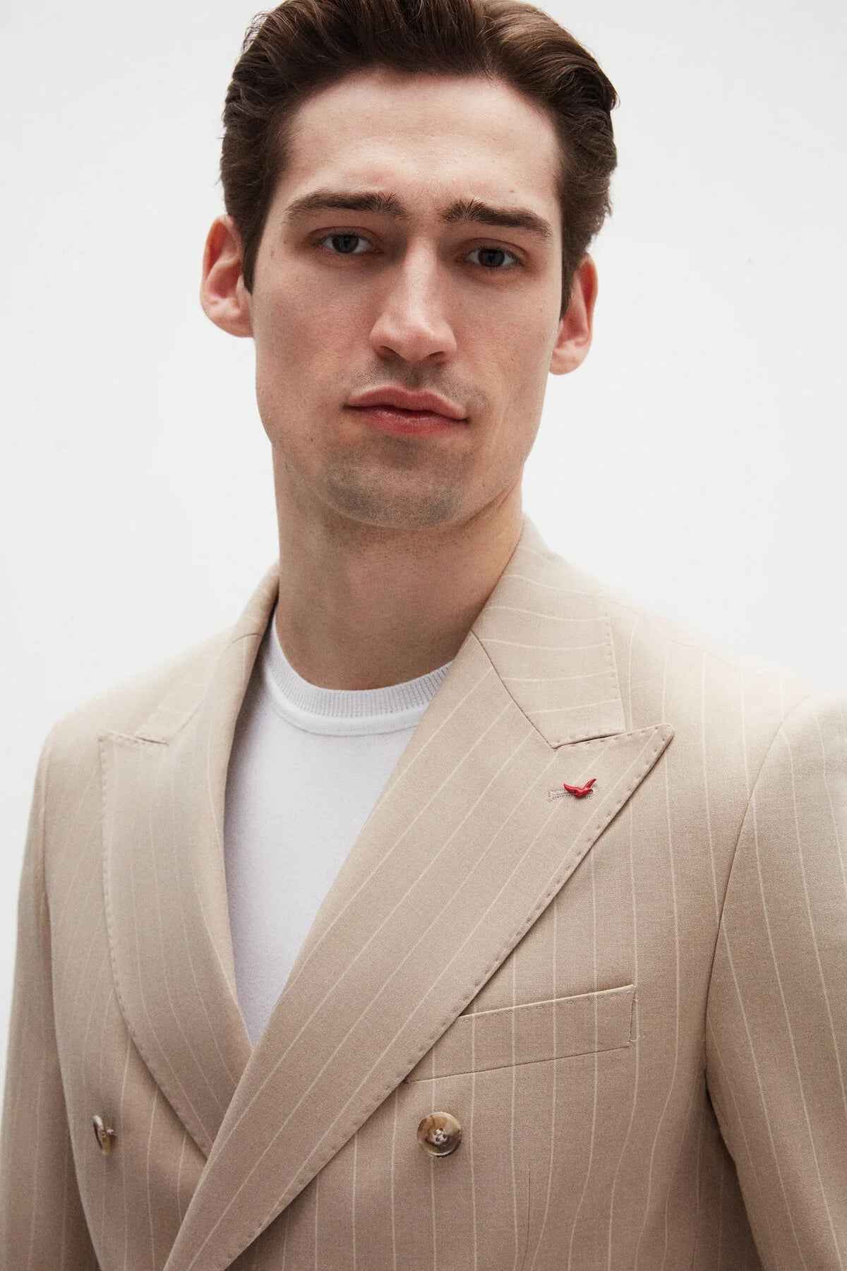 Beige striped men’s blazer with pocket square and gold-tone button details on lapel.
