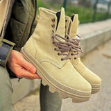 Men's beige suede lace-up boots held in hand, side view