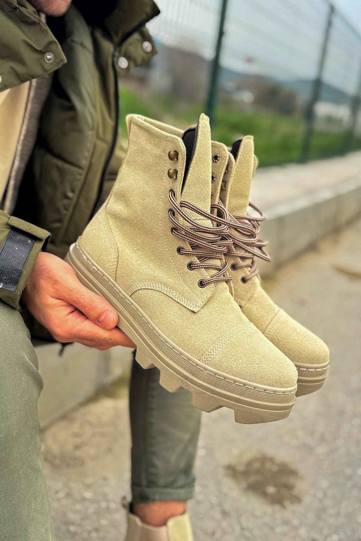 Men's beige suede lace-up boots held in hand, side view
