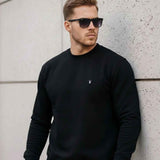 Black crewneck sweatshirt with long sleeves and small chest logo, ribbed hem