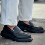 Black loafers on tiled pavement, front three-quarter view with strap