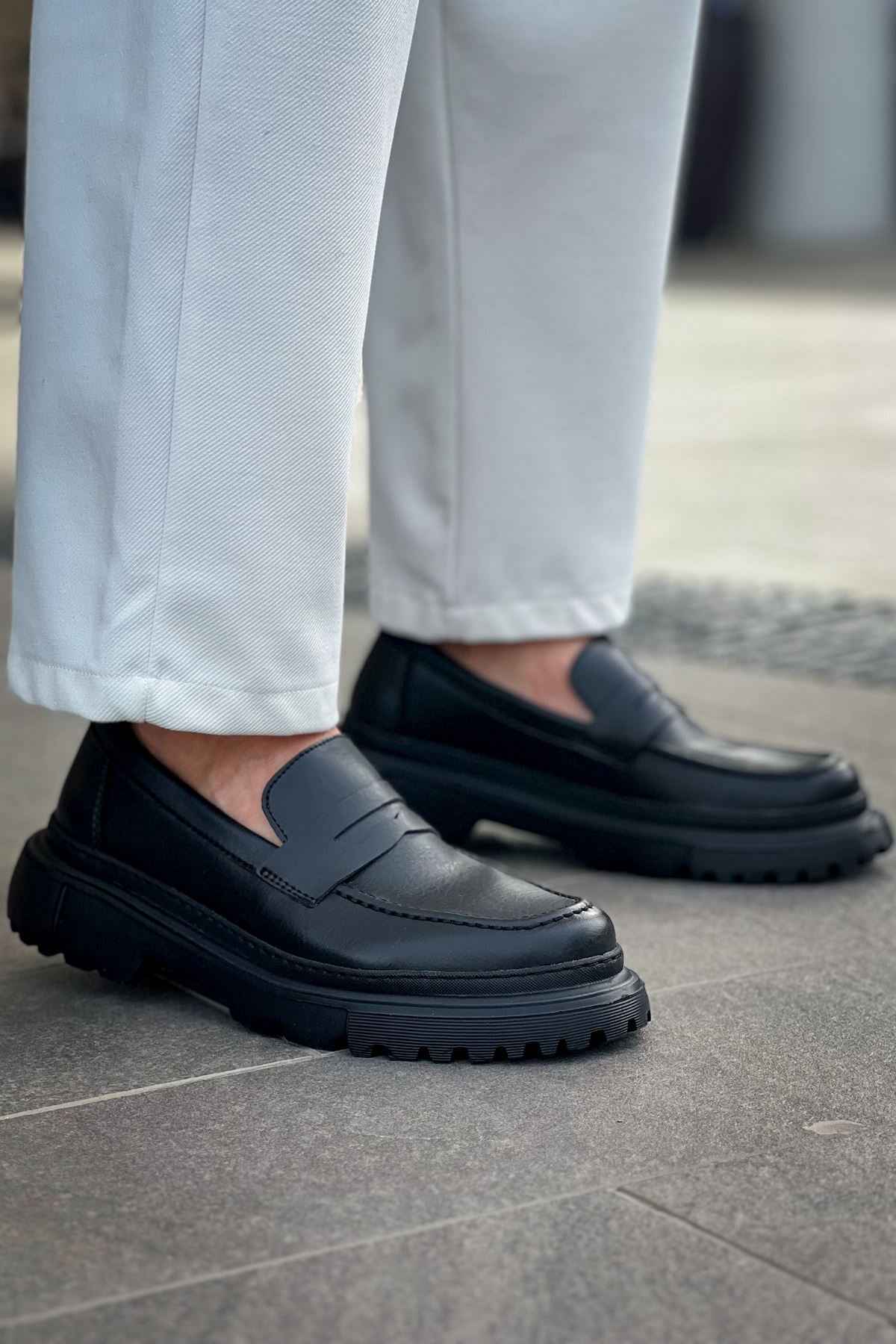 Black loafers on tiled pavement, front three-quarter view with strap