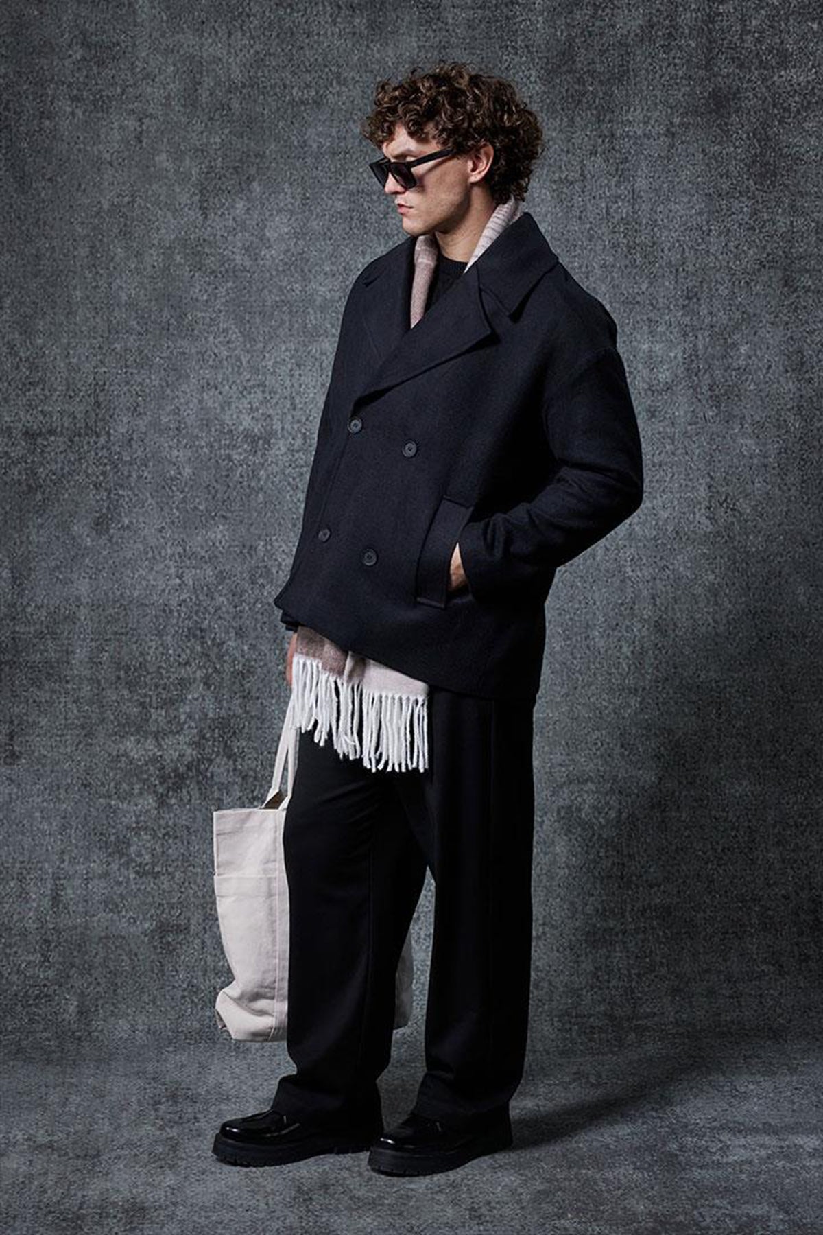 Men's oversized black double-breasted coat with flap pockets and fringed hem detail.