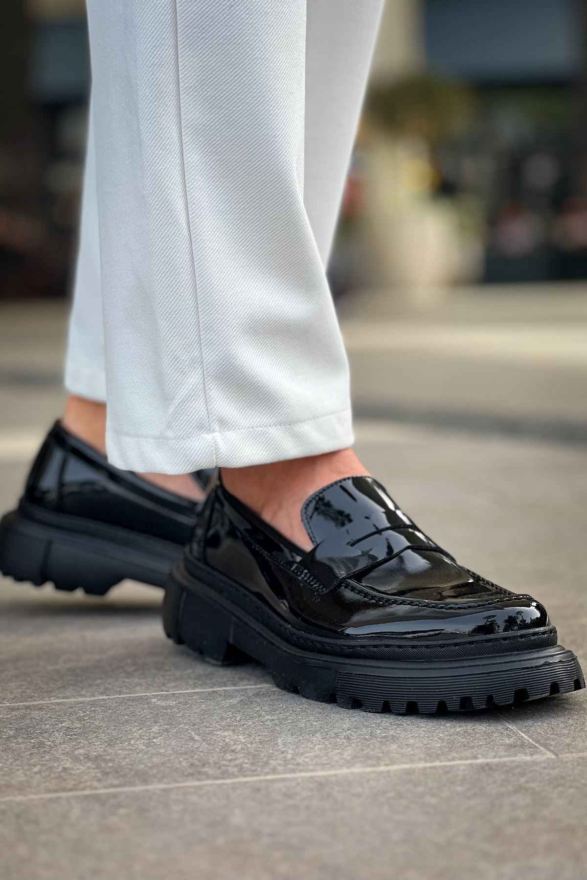 Black patent leather loafer with chunky tread sole and strap detail, side view