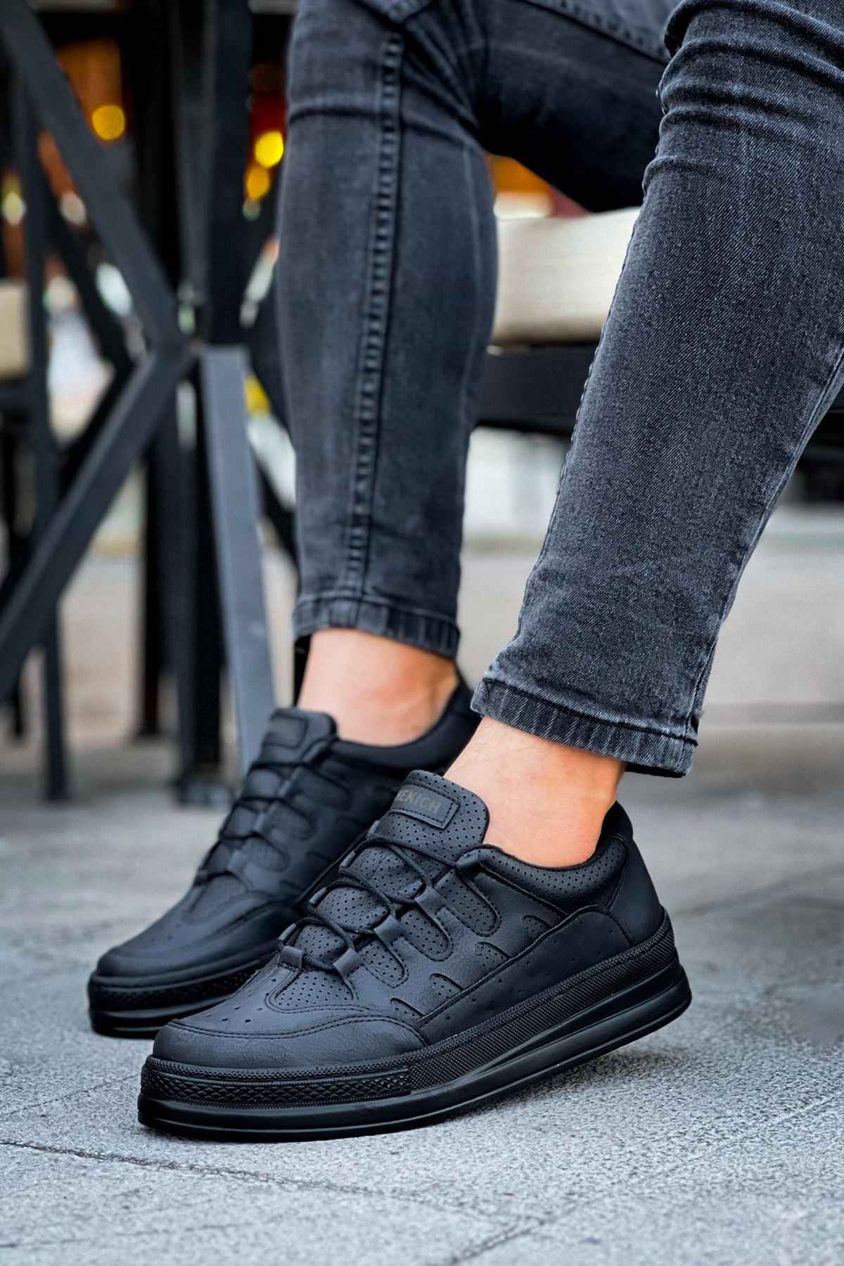 Men's black sneakers, lace-up front and side panels, worn with cuffed jeans