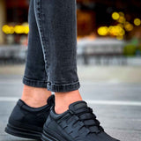 Men's black sneakers with lace-up vamp and textured overlays, side view with jeans