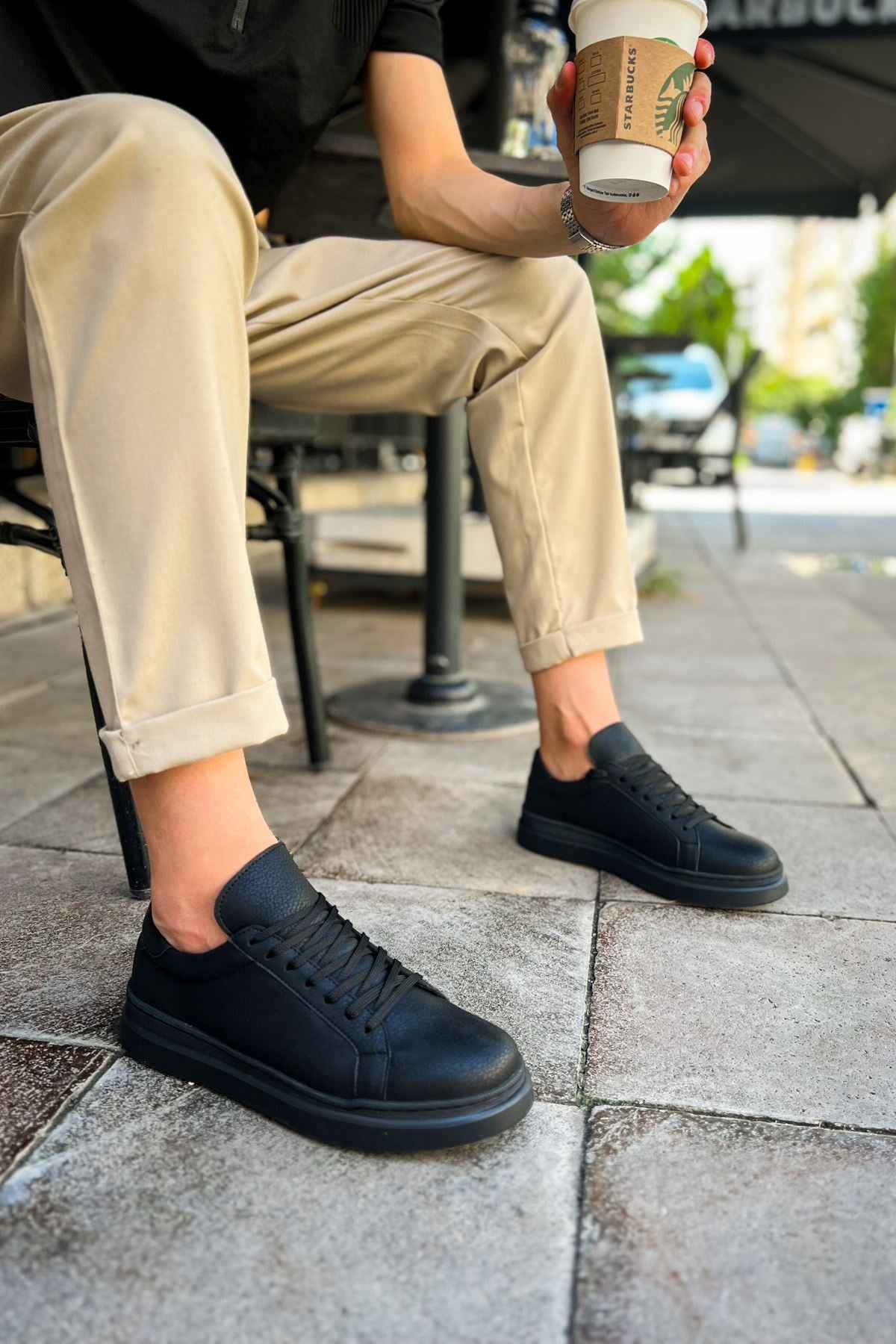 Black lace-up sneakers on feet, low profile with textured upper