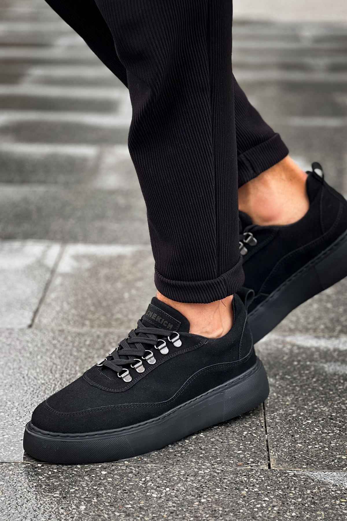 Black suede sneakers with low profile, silver eyelets, and rubber sole