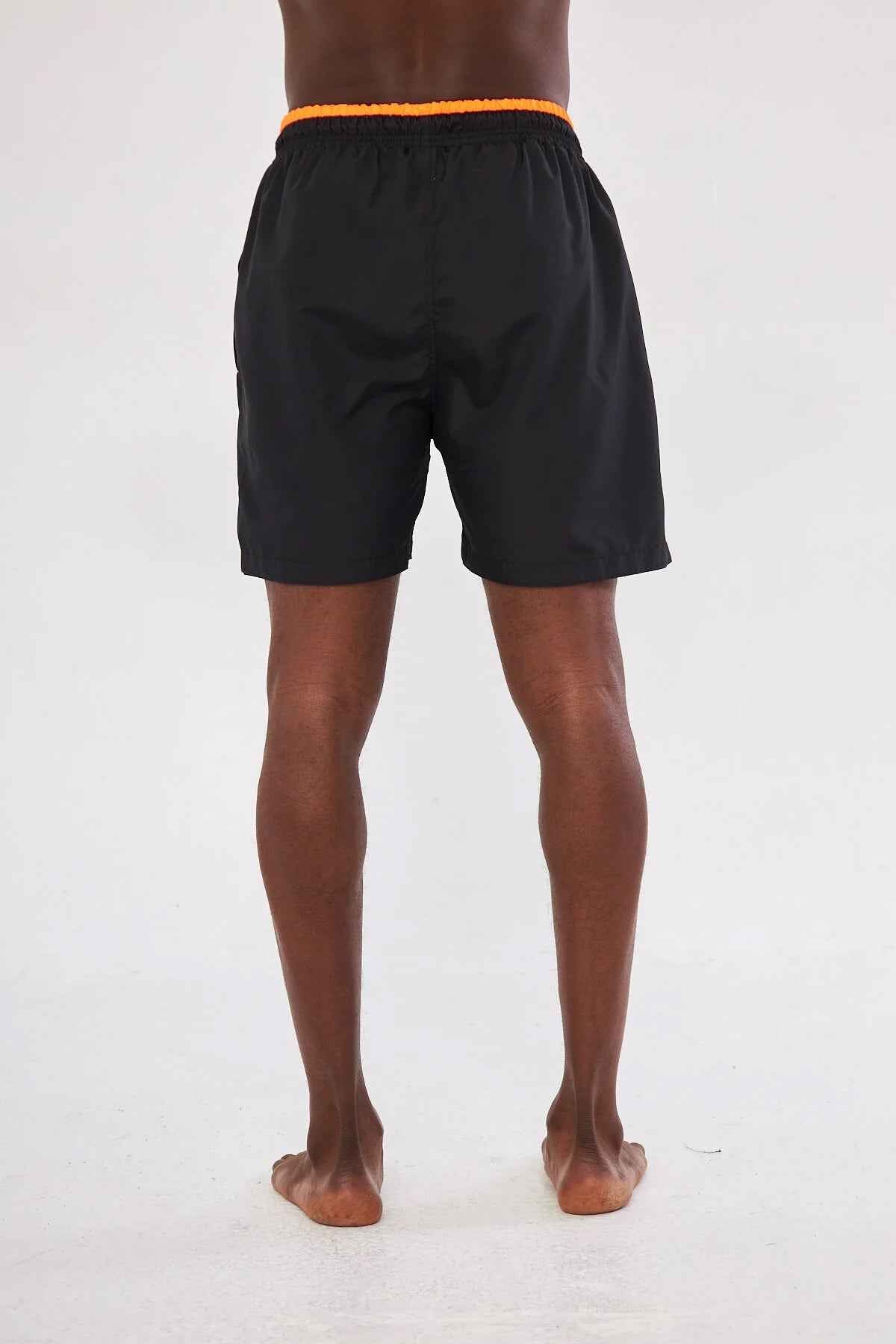 Men's black swim shorts back view with orange waistband trim and elastic hem.