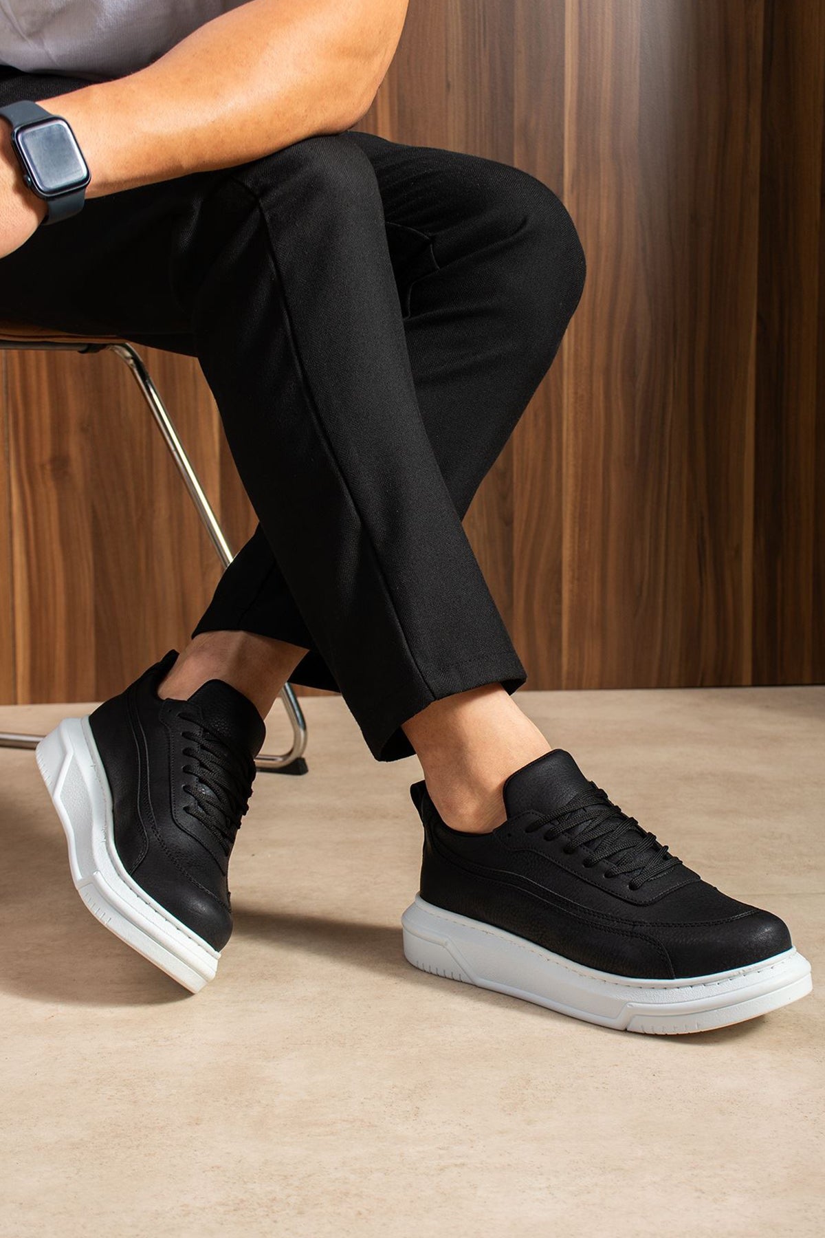 Black lace-up sneakers with white sole, profile view with bent leg