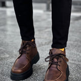 Pair of men's brown lace-up ankle boots standing on street pavement, dark soles