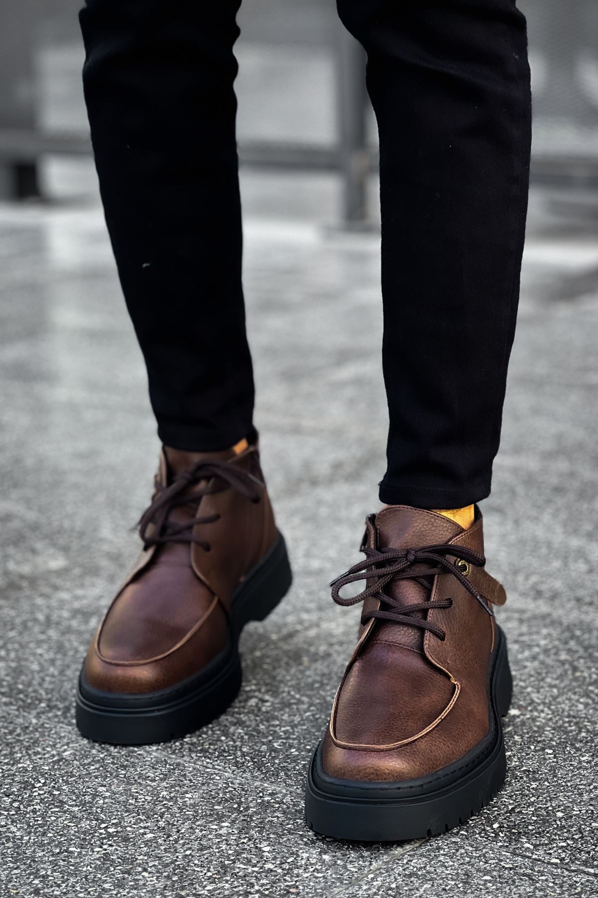 Pair of men's brown lace-up ankle boots standing on street pavement, dark soles