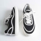 Black canvas low-top sneakers with white laces, trim panel, and thick white sole