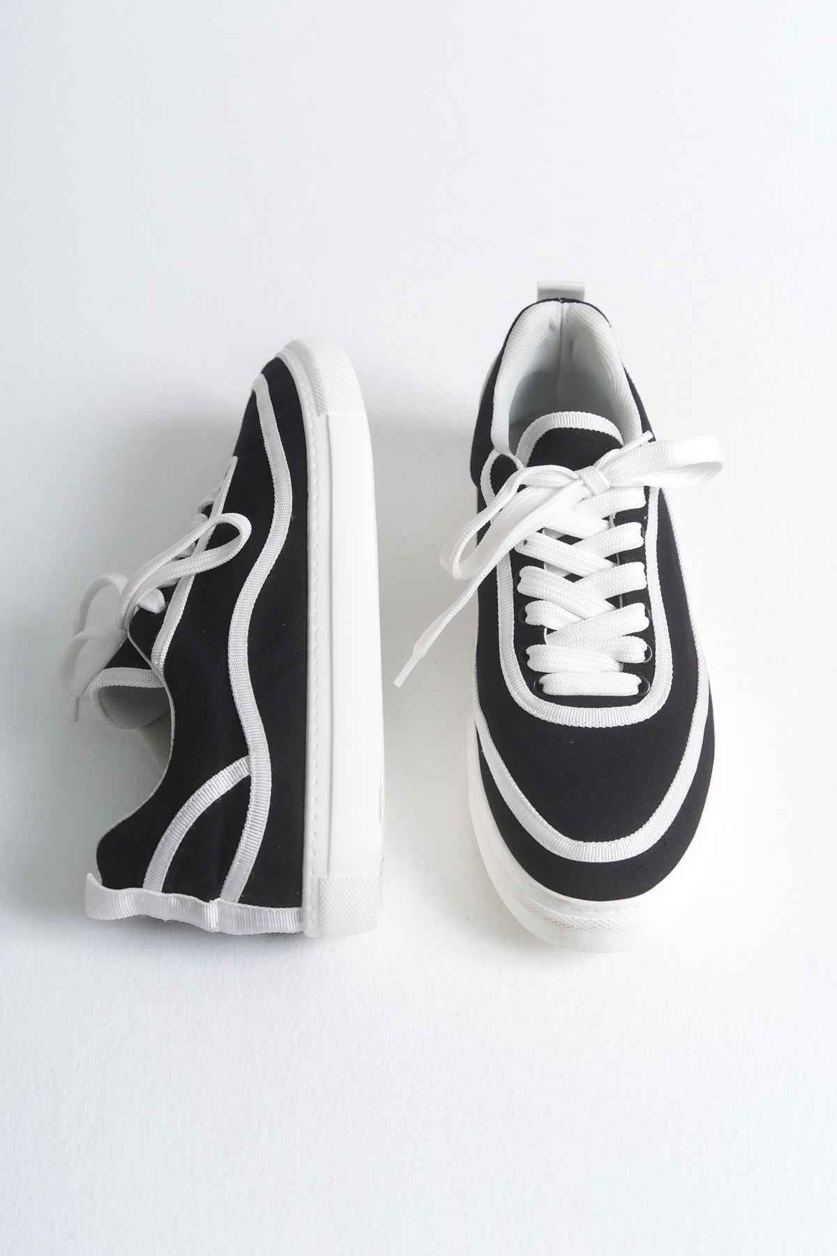 Black canvas low-top sneakers with white laces, trim panel, and thick white sole