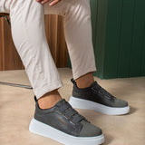 Pair of dark gray casual sneakers on feet with white rubber sole and strap closure