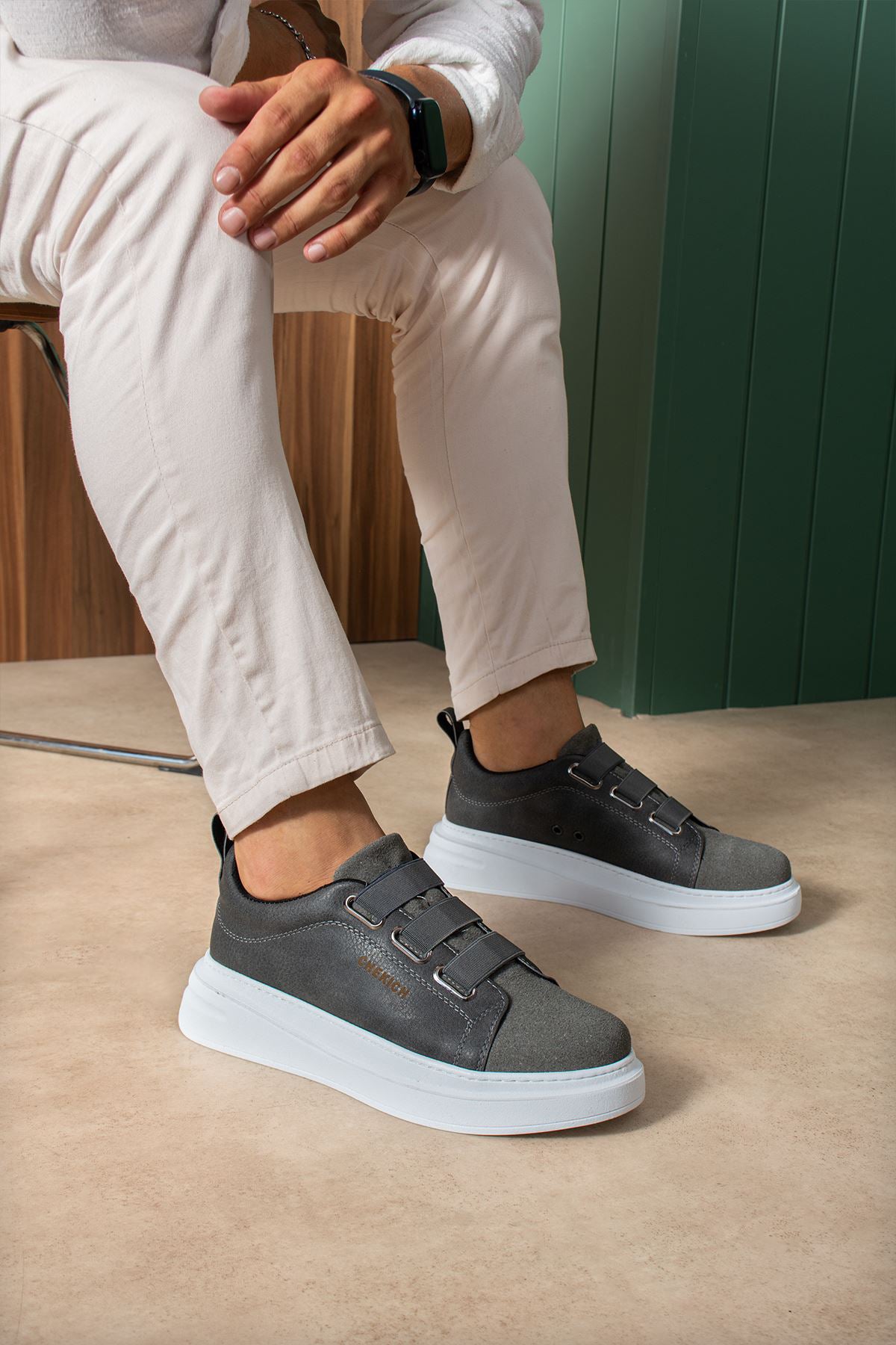 Pair of dark gray casual sneakers on feet with white rubber sole and strap closure