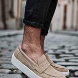 Beige suede slip-on loafers with strap detail and white textured sole.