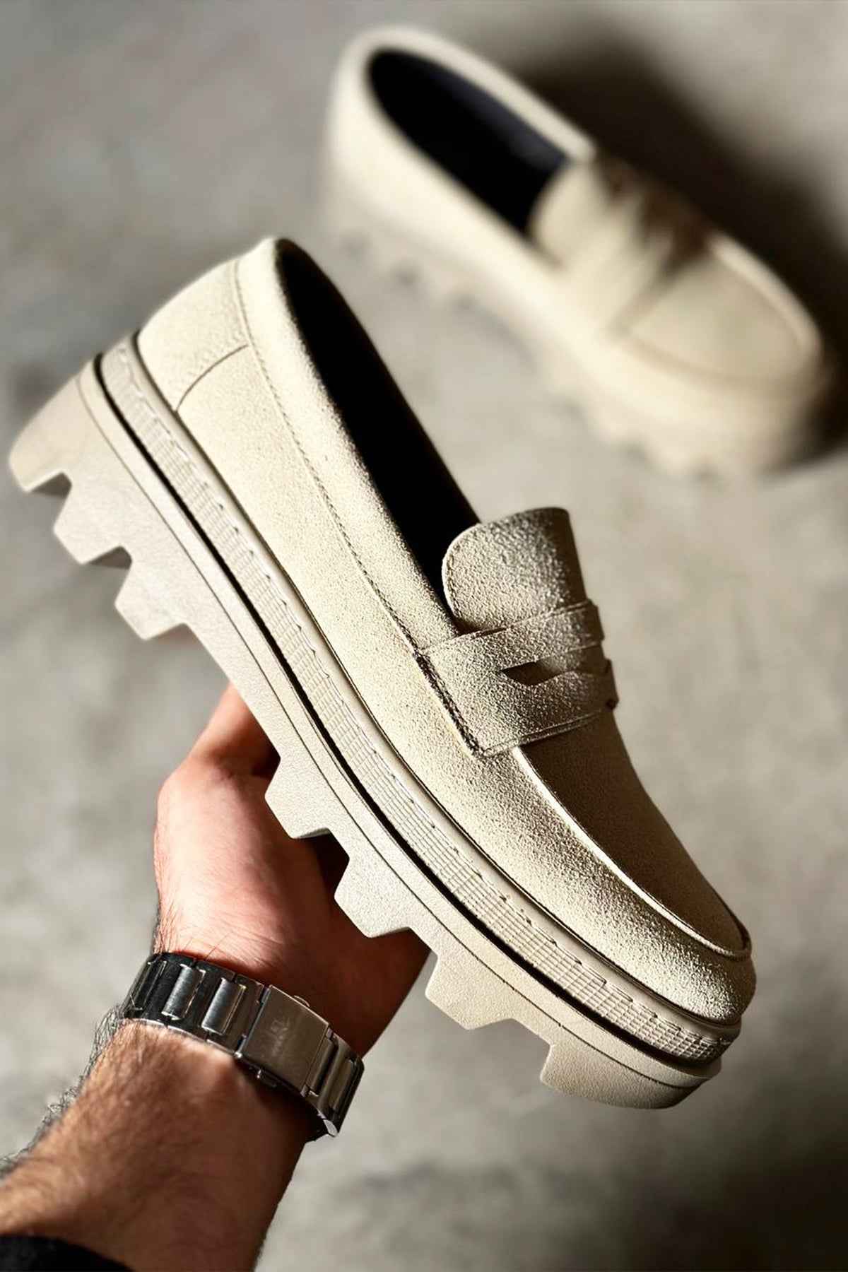 Men's beige suede loafer with strap vamp and contrast stitching, held in hand