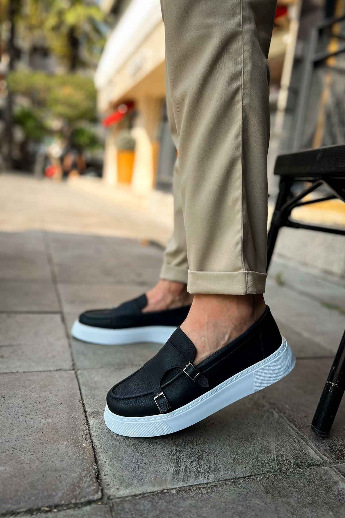 Black slip-on loafers with buckle strap and light blue sole, front view