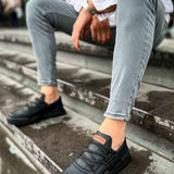 Men's black low-top sneakers on a paved step, worn with light blue jeans