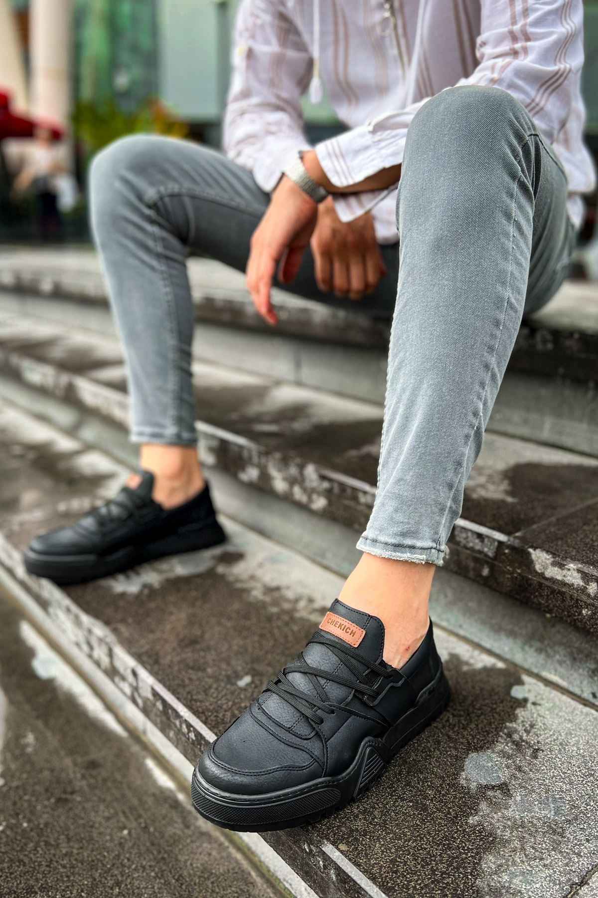 Men's black low-top sneakers on a paved step, worn with light blue jeans