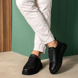 Black casual sneakers on feet, curved side panels and low rubber sole