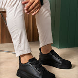Black low-top sneakers on feet with side strap detail and rounded toe