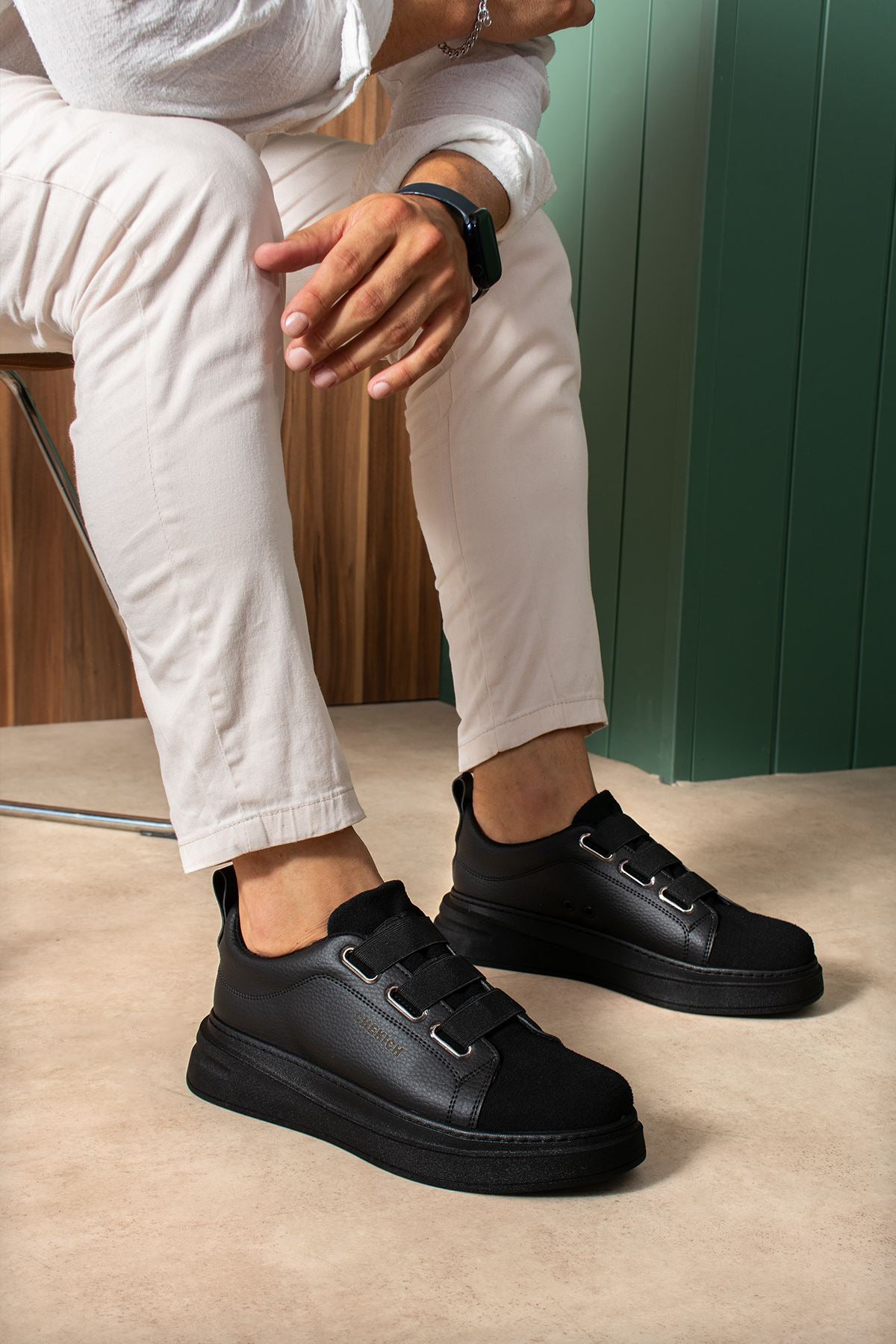 Black low-top sneakers on feet with side strap detail and rounded toe