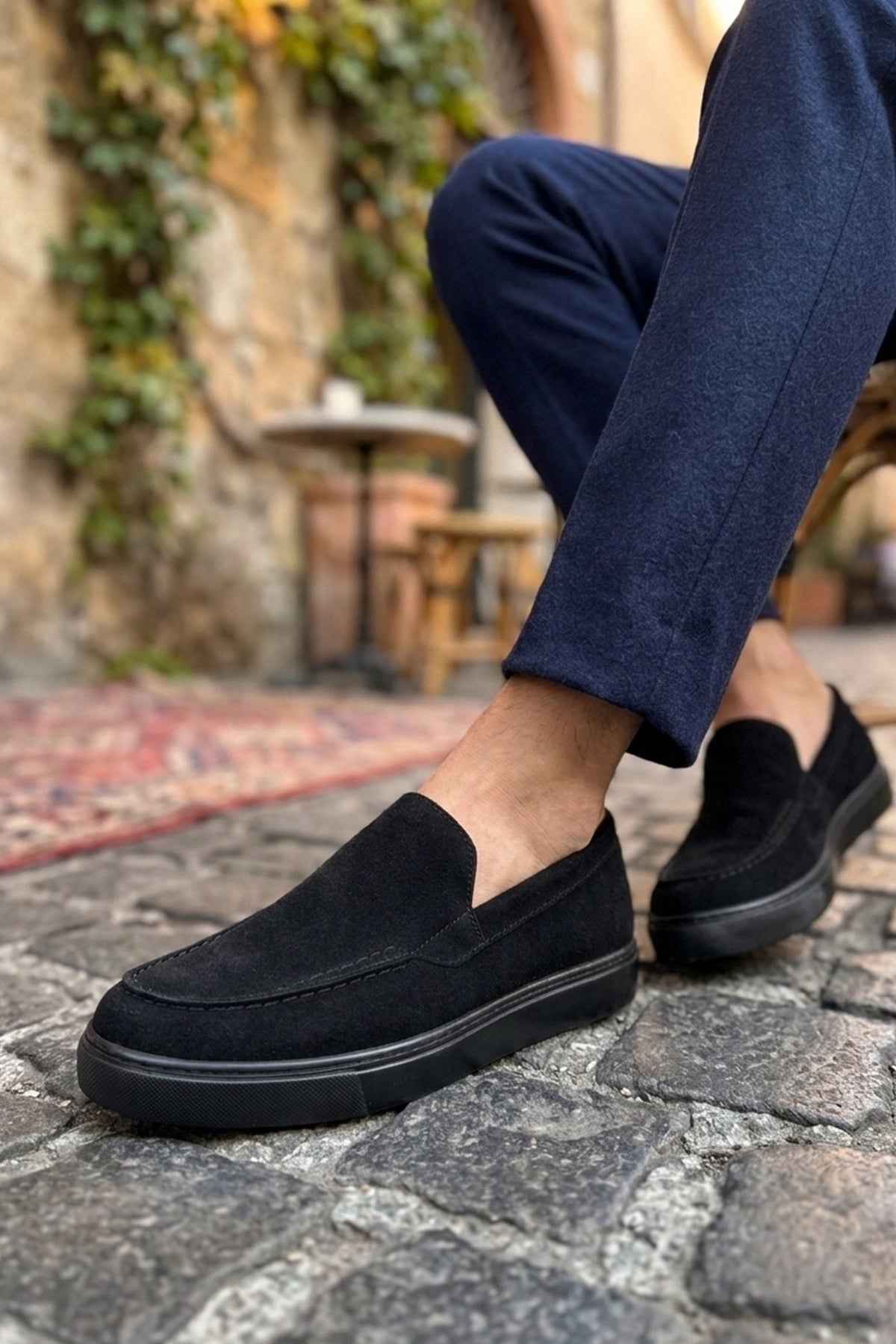 Men's black suede loafers on foot, slip-on style with side panel detail