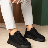 Men's black suede lace-up sneakers, front view on model with light pants.