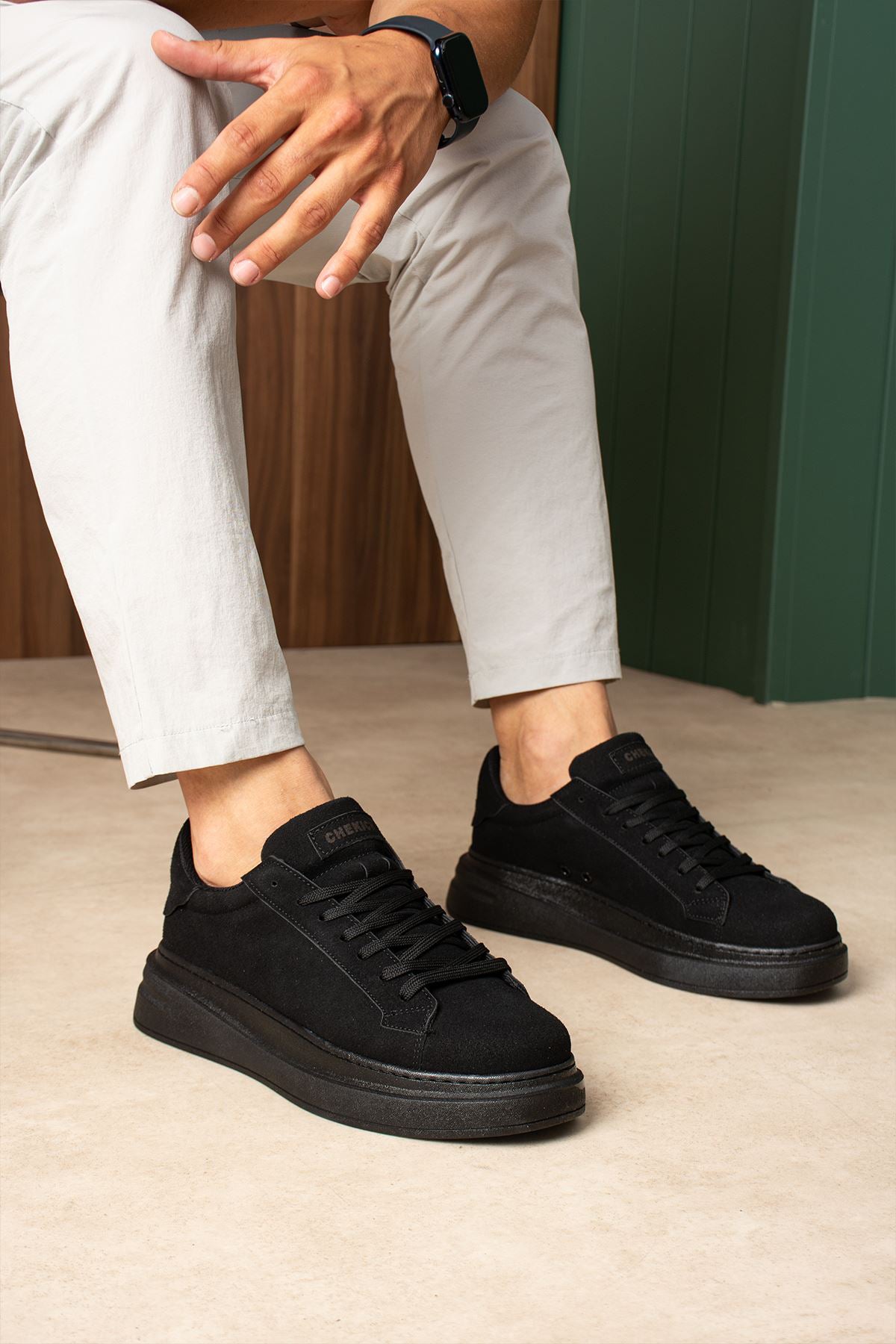 Men's black suede lace-up sneakers, front view on model with light pants.