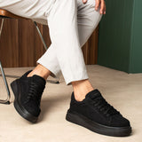 Men's black suede lace-up sneakers on feet, low profile with rubber sole.