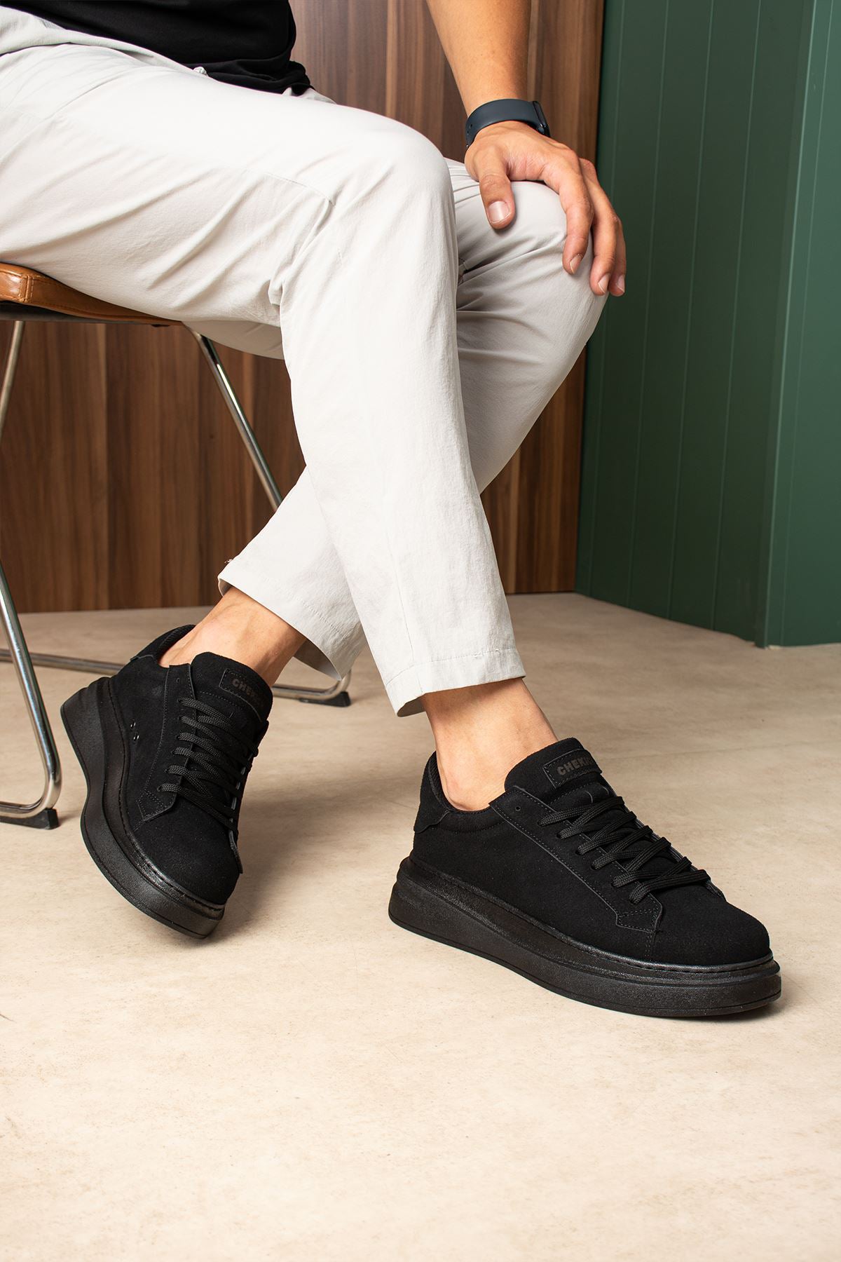 Men's black suede lace-up sneakers on feet, low profile with rubber sole.