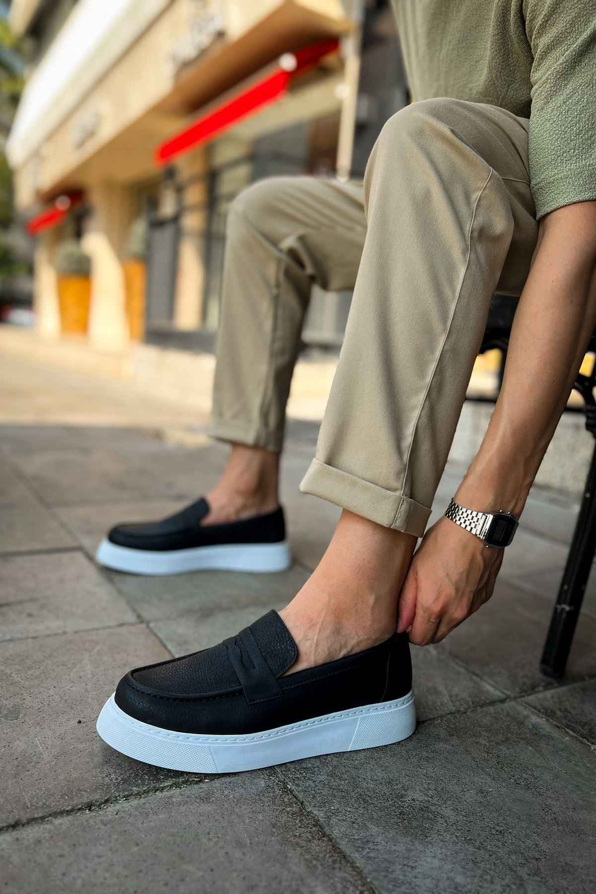 Men's black slip-on loafers with white soles, worn with cuffed pants