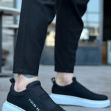 Black slip-on sneakers with white sole and side logo text