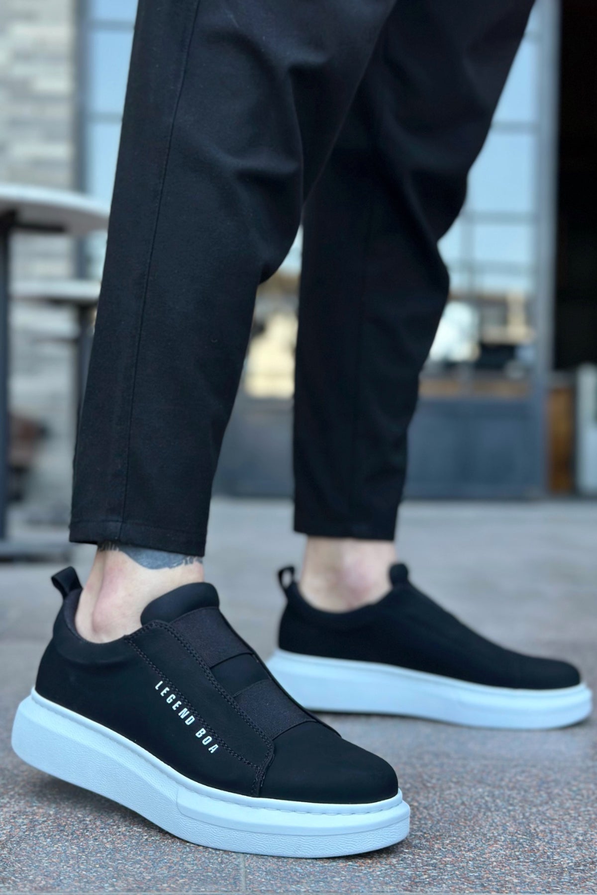 Black slip-on sneakers with white sole and side logo text