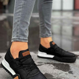 Black low-top sneakers with black laces and tan side panels, white rubber sole