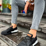 Black lace-up sneakers with tan accent patch and white sole, low-top style
