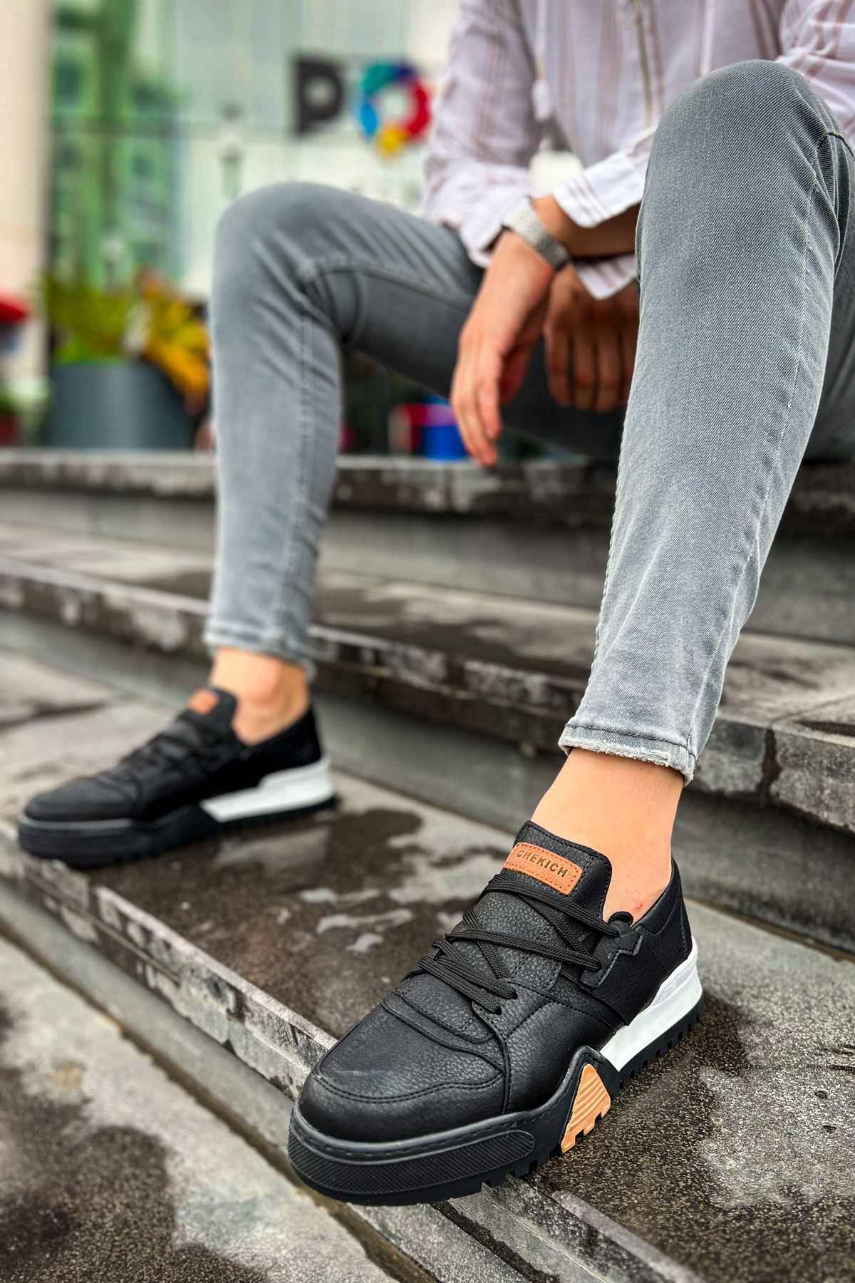 Black lace-up sneakers with tan accent patch and white sole, low-top style
