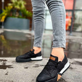 Black low-top lace-up sneakers with tan heel tab and white midsole, side view