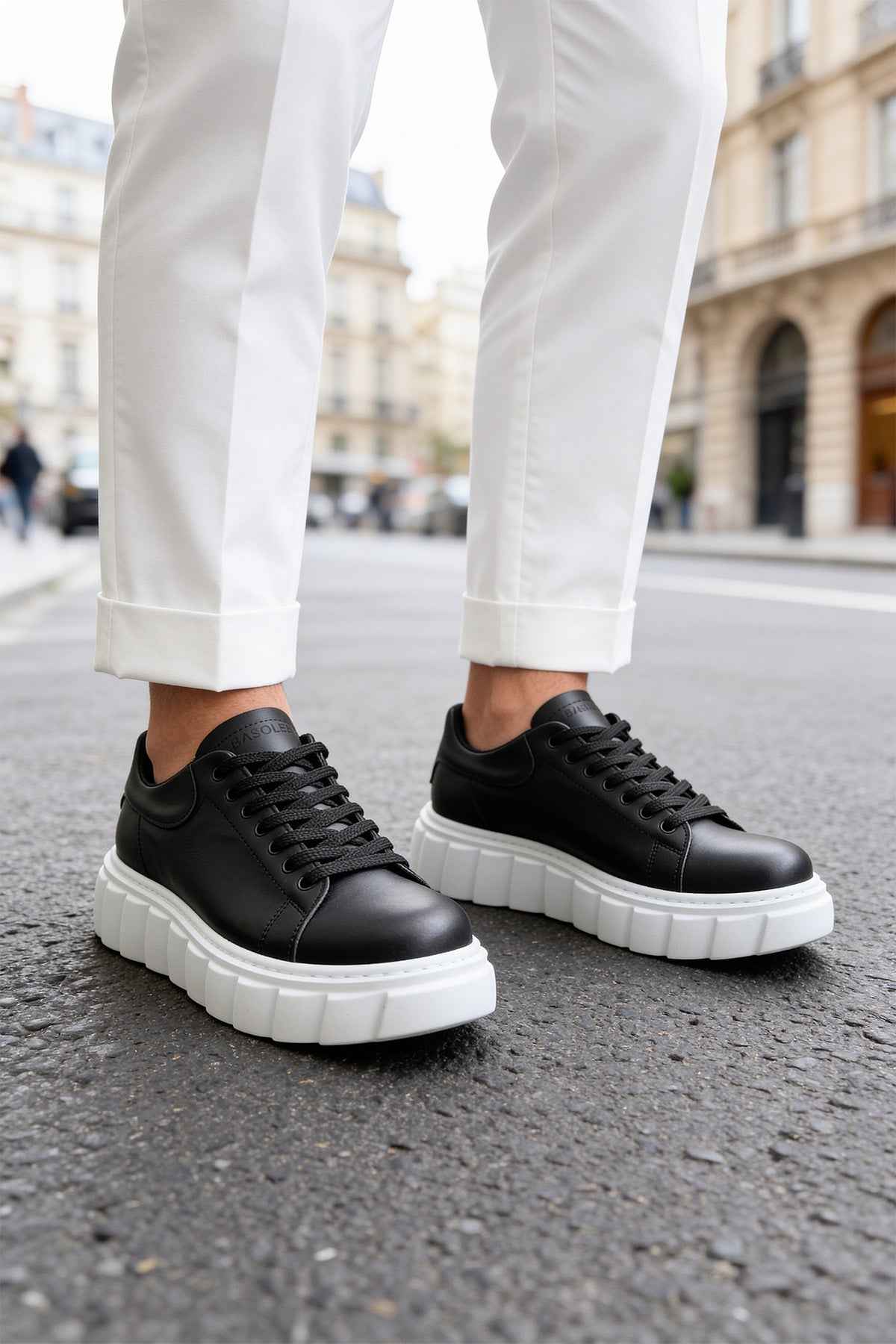 Black lace-up sneakers with white platform soles, worn with cuffed pants
