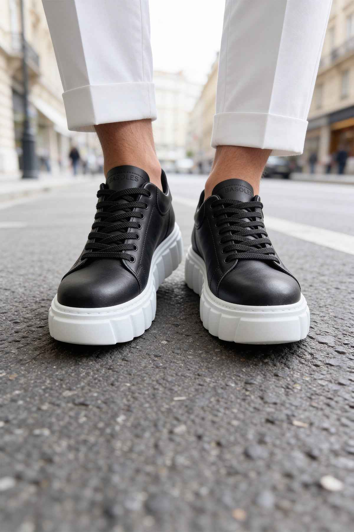 Black lace-up sneakers with white soles, close-up of sides and stitching